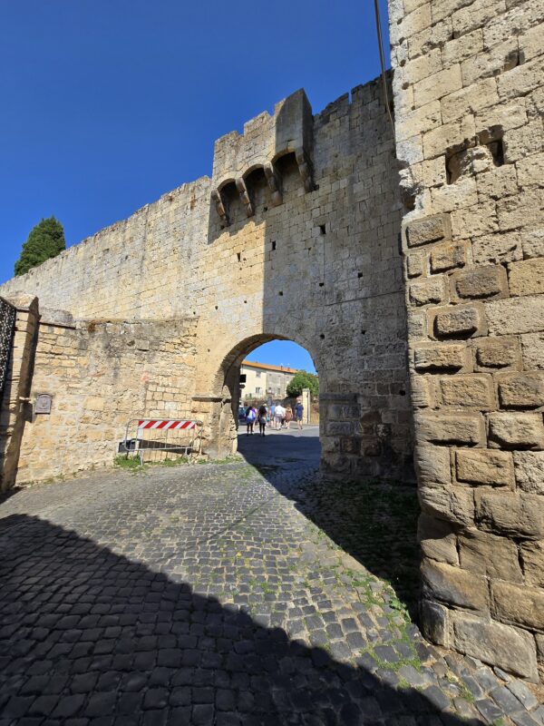 A massive stone archway forming part of Tarquinia’s medieval walls, with sunlight casting shadows on the cobblestone street.