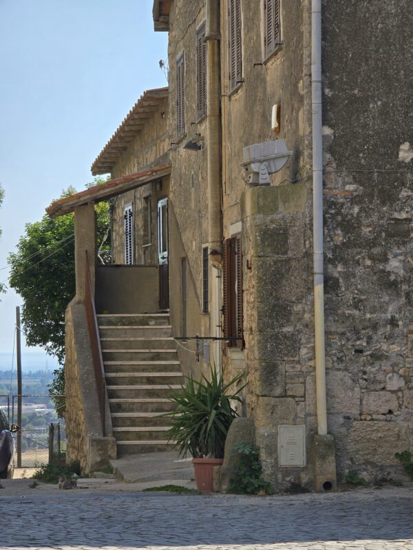 A weathered stone house in Tarquinia with wooden shutters, exterior stairs, and a potted plant, capturing the town’s lived-in medieval charm.