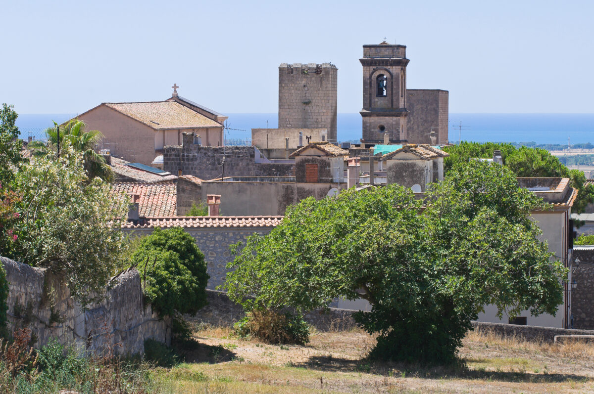 View of Tarquinia, Italy, showing rooftops, a medieval tower, and a bell tower with the Tyrrhenian Sea in the background.