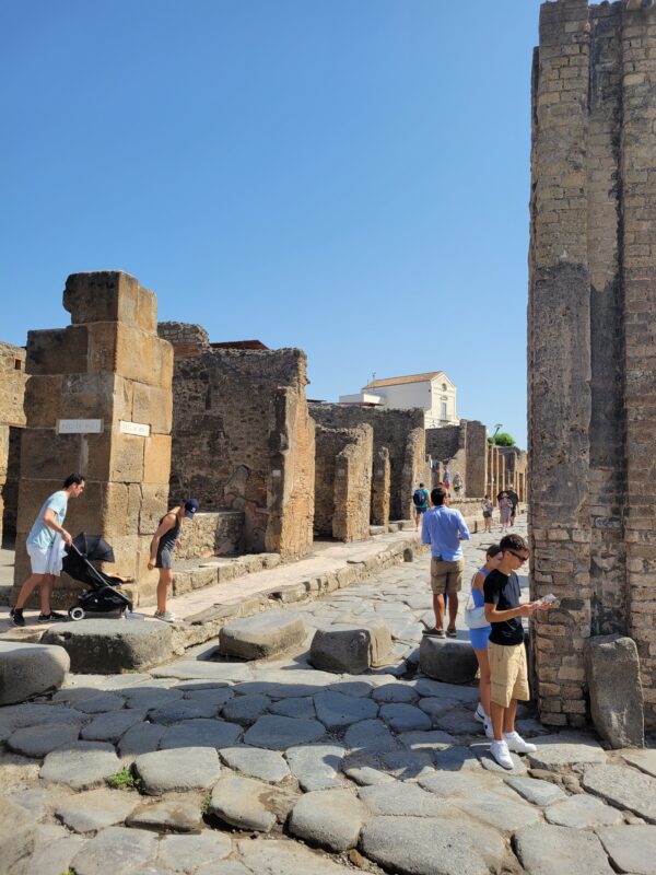 Ancient stone streets and ruins of Pompeii with visitors exploring, a popular shore excursion from the Naples cruise port.