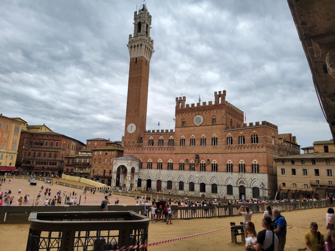Wide view of Siena’s historic central square with medieval brick buildings and tower under a cloudy sky.