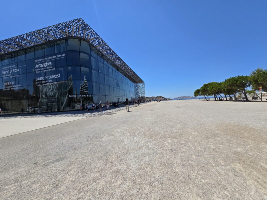 Marseille waterfront with a modern museum, historic buildings, and a harbor filled with small boats under a clear blue sky.