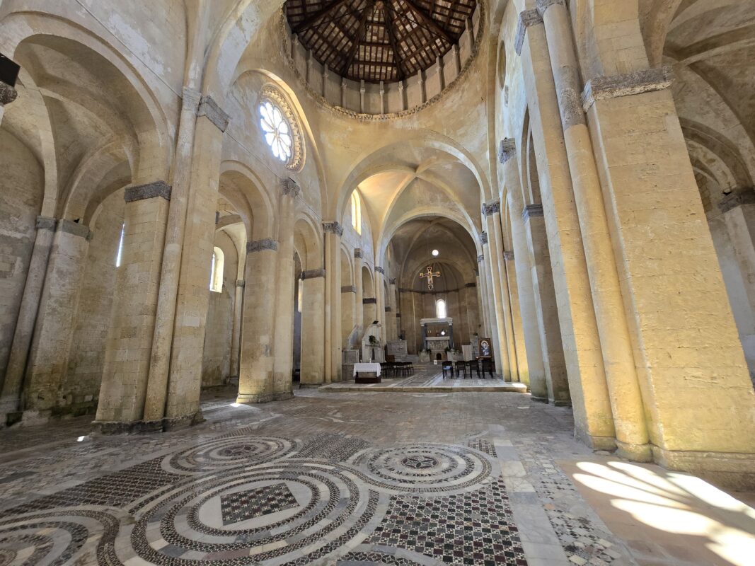 Interior of Tarquinia Cathedral in Italy, with stone arches and mosaic floor patterns, a closer alternative to Rome excursions from the Civitavecchia cruise port.