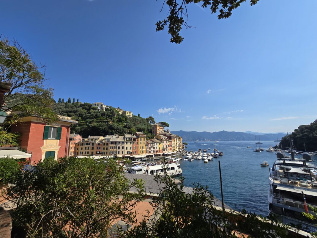 View of Portofino’s waterfront and Ligurian coastline, featuring yachts and pastel harbor buildings.