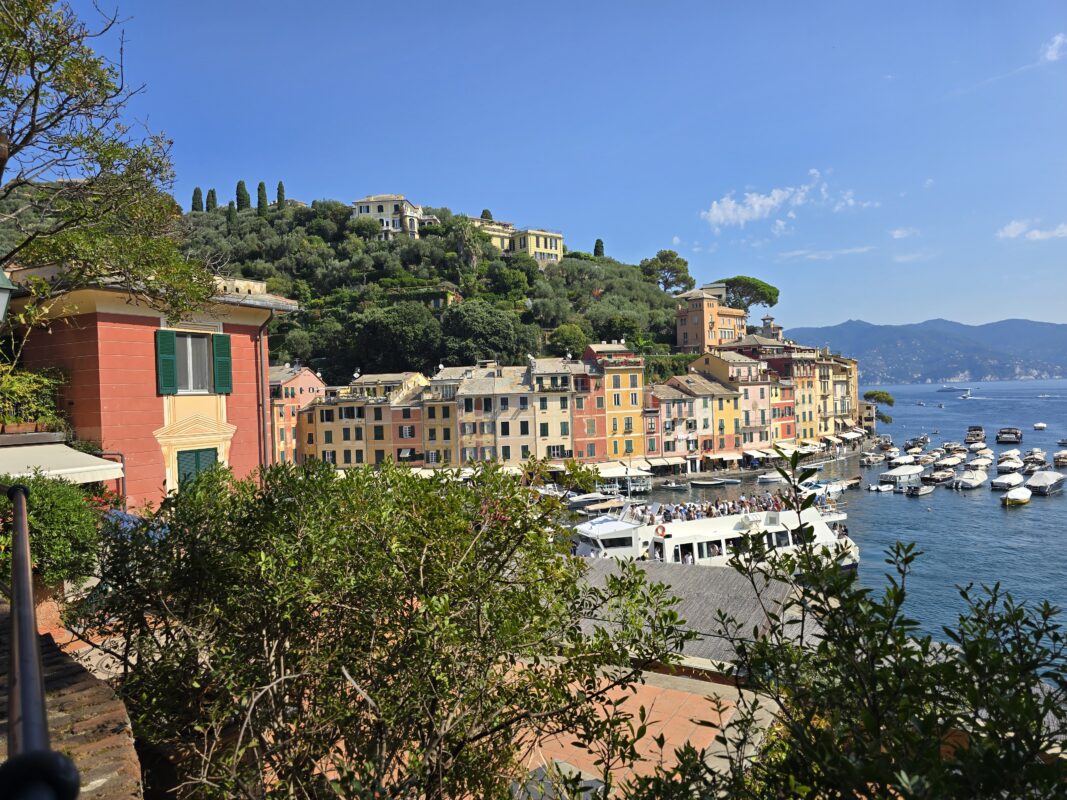 Mediterranean hillside village overlooking a harbor, with stacked houses and lush greenery above the sea.