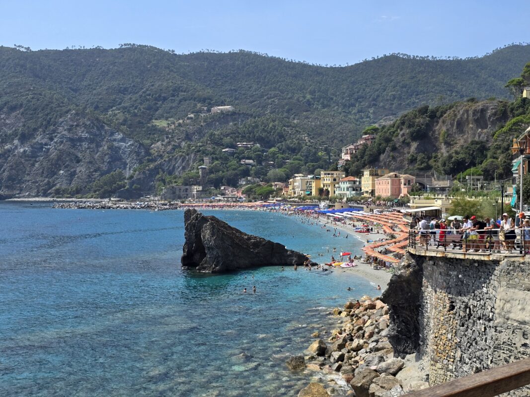 Seaside scene in Monterosso showing the long sandy beach, pastel buildings, and rugged hillsides.