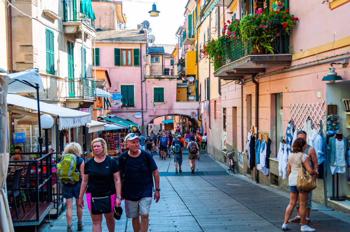Tourists wander through a lively Monterosso street lined with shops, flowers, and colorful facades.