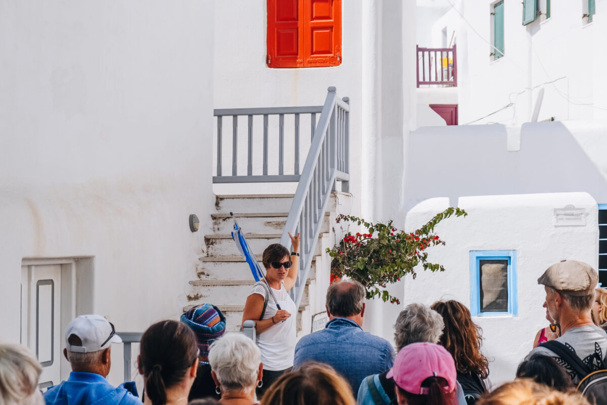 Tour guide leading a small group through narrow whitewashed streets with colorful shutters in a Mediterranean village.