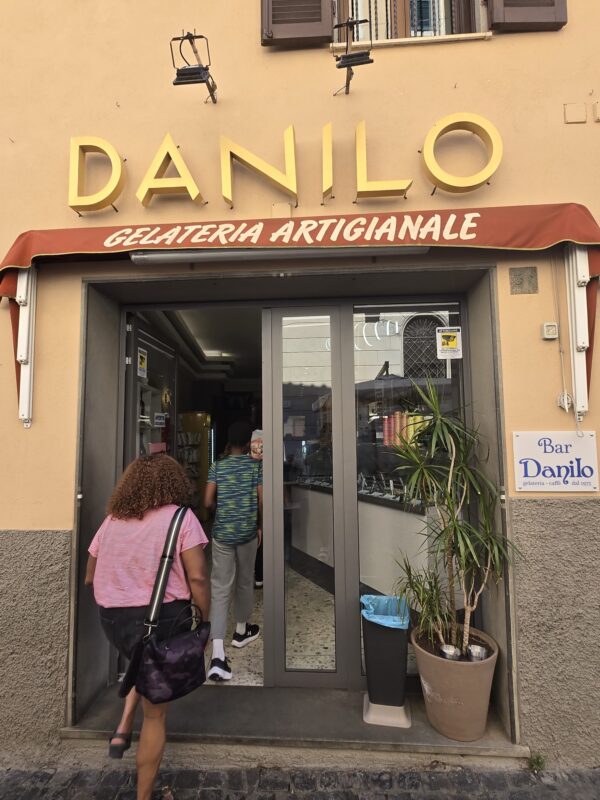 View of Gelateria Danilo storefront, with customers entering under a sign advertising handmade gelato.