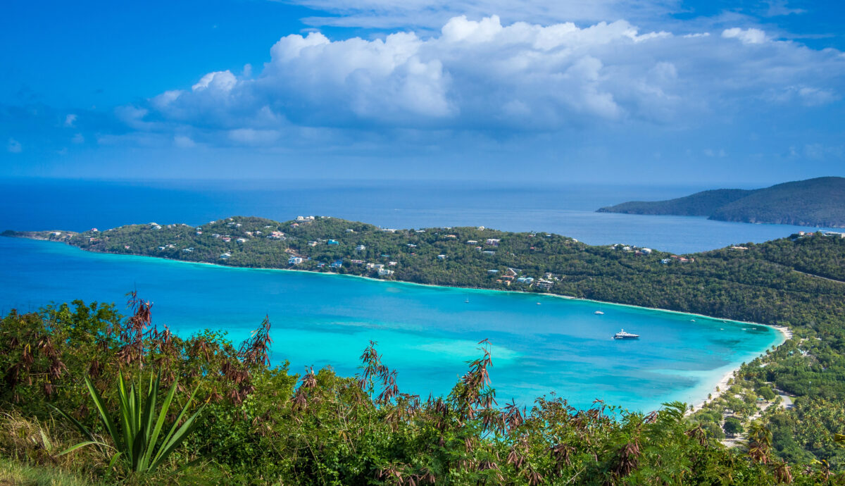 A panoramic view of Magens Bay on St. Thomas, U.S. Virgin Islands, showing bright turquoise water curving along a white sandy beach backed by green hills and dotted with boats.
