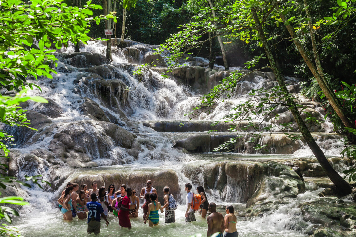 Group of people wading and climbing limestone terraces beneath cascading water at Dunn’s River Falls in Jamaica.