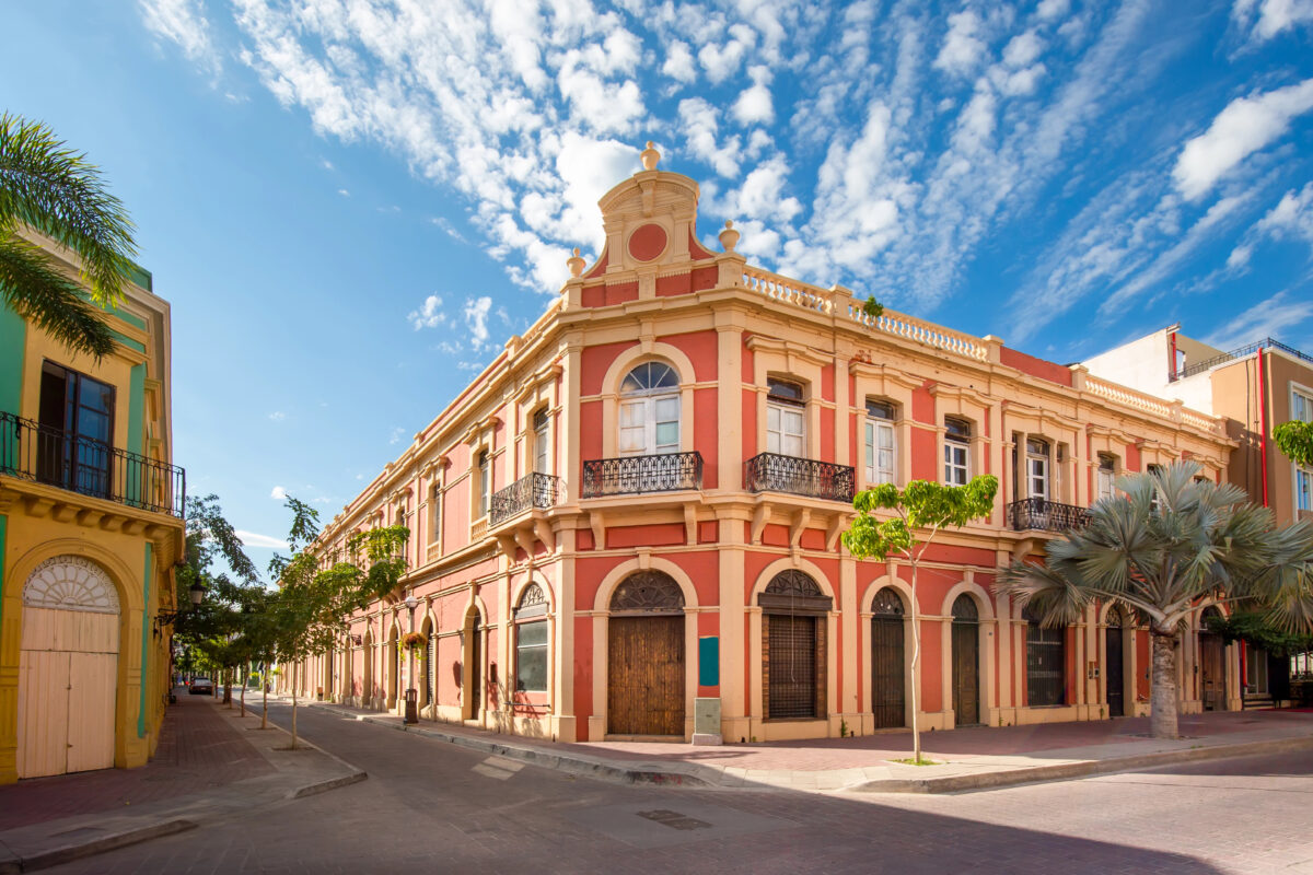 Corner view of a red and yellow colonial-era building in Old Mazatlán surrounded by quiet streets and tropical plants.