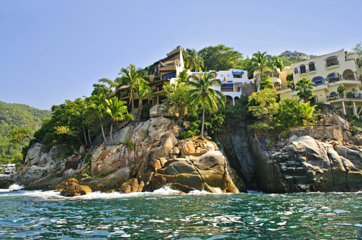 Ocean view of Puerto Vallarta’s southern coastline with palm trees, villas, and rocky cliffs rising above the Pacific water.