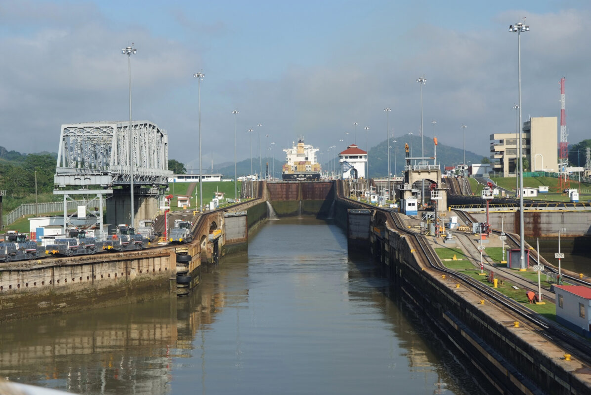 Cargo ship entering the Miraflores Locks of the Panama Canal with surrounding machinery and rail lines visible.