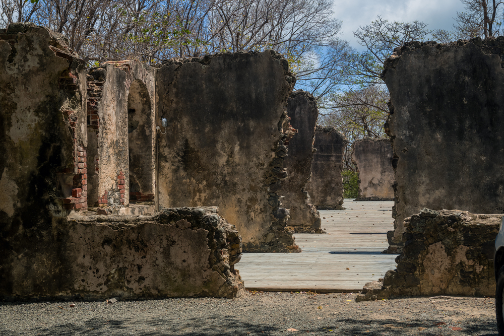 Sunlit ruins with crumbling stone and brick walls, archways, and bare trees behind, located at Morne Coubaril Estate in St. Lucia.