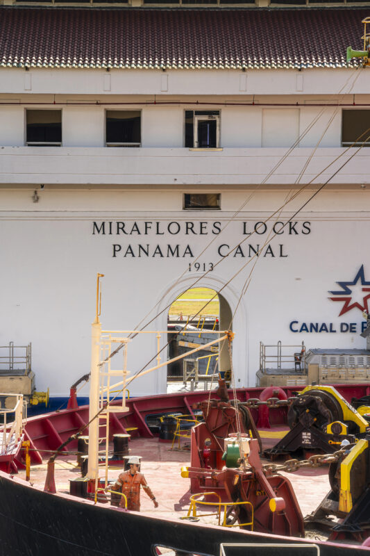 Close-up view of the Miraflores Locks building at the Panama Canal with a ship and crew visible in the foreground.
