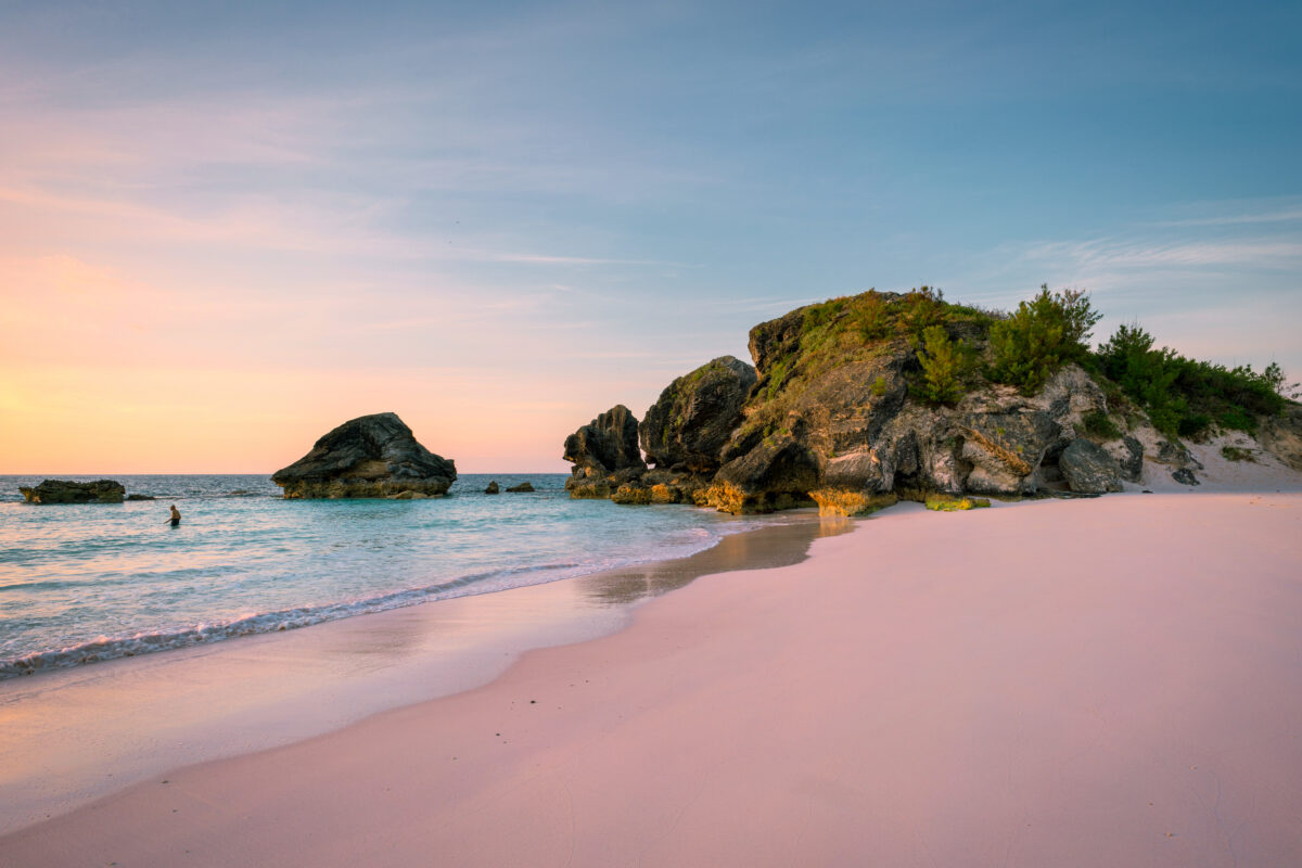 Scenic view of Horseshoe Bay Beach in Bermuda with pink-tinted sand, ocean waves, and limestone rocks along the shore.