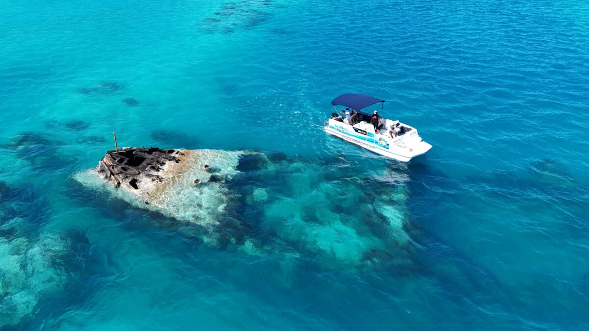 Overhead view of a small boat floating above a visible shipwreck in Bermuda’s bright blue water, known for snorkeling tours.