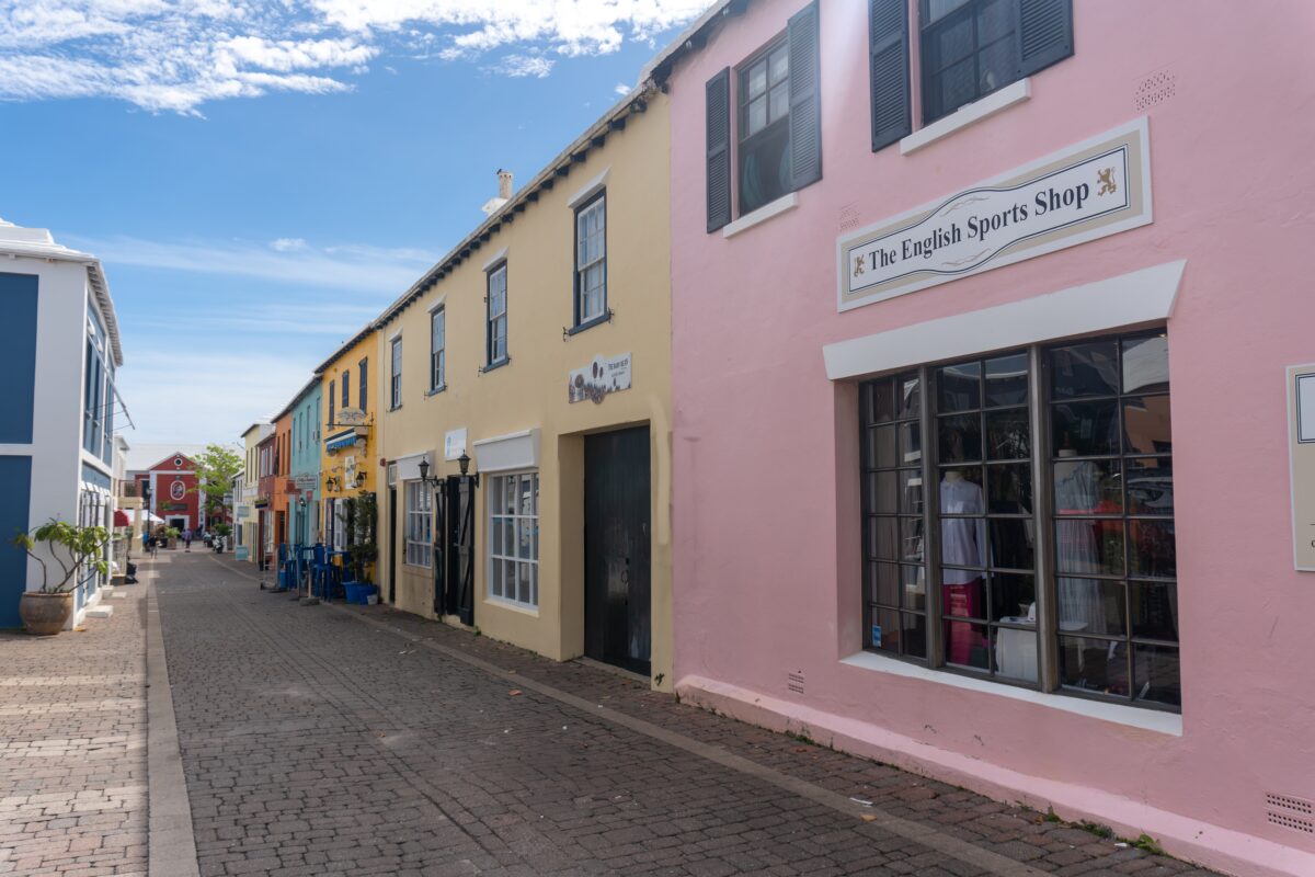 Colorful pastel buildings and boutique shops along a cobblestone street in St. George’s, Bermuda, under a bright blue sky.