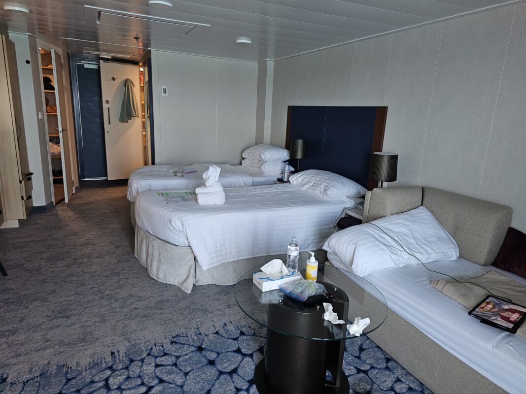 Junior suite on a cruise ship with two twin beds, sofa bed, and open layout showing extra space and modern furnishings.