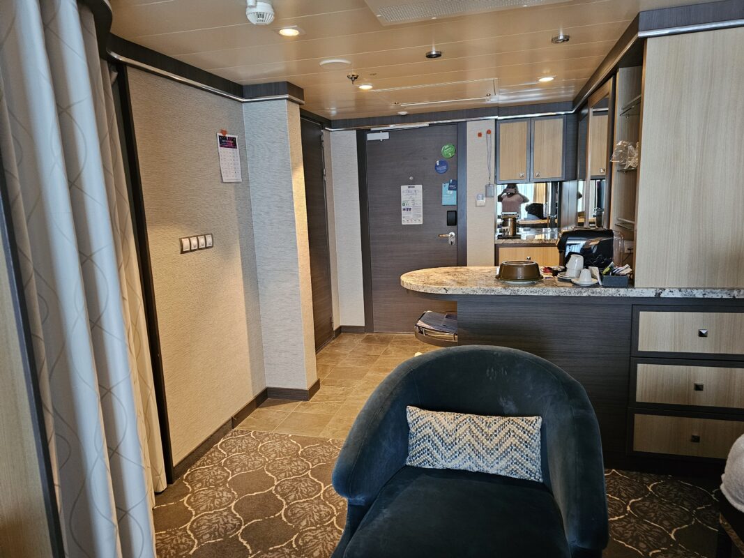 Cruise ship suite interior with marble countertop bar, modern cabinetry, and seating area, showing upgraded finishes and open layout.