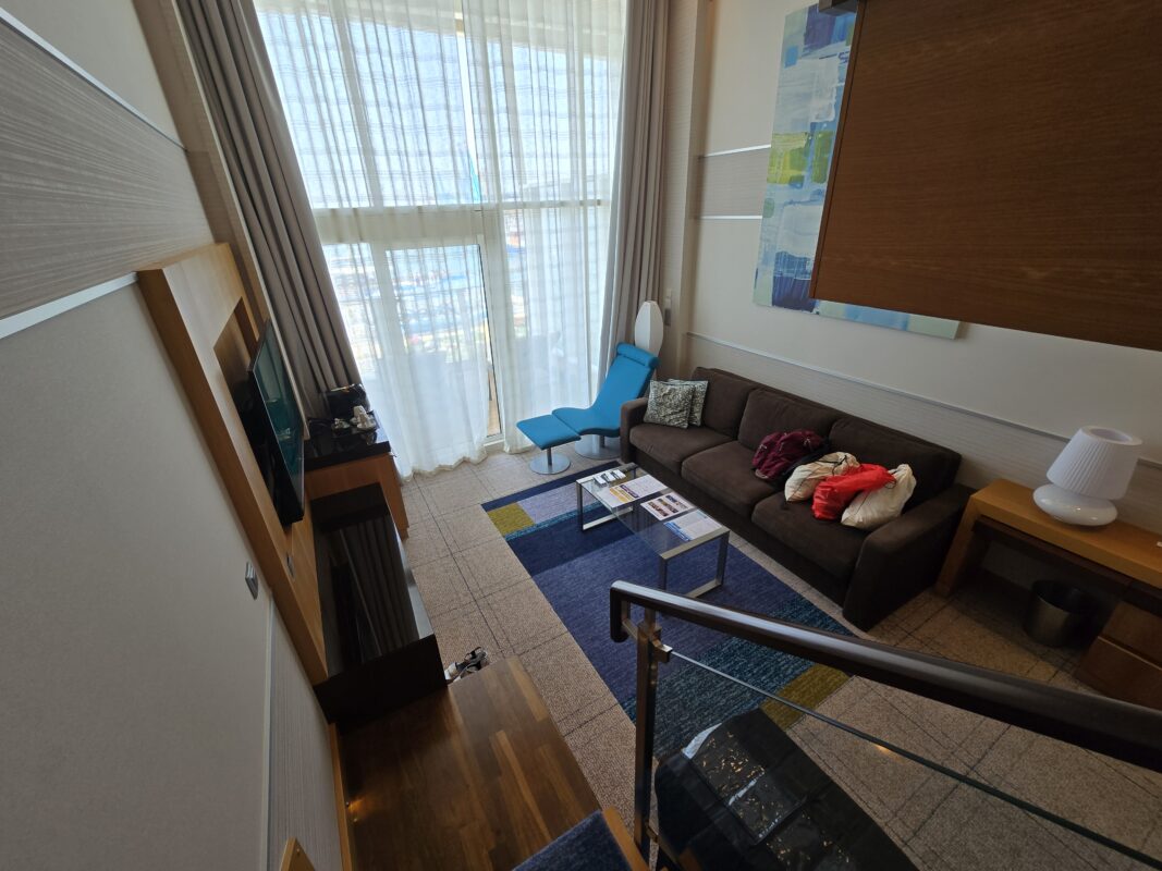Interior of a Royal Caribbean two-level Crown Loft Suite booked through the Royal Caribbean Royal Up program, featuring a modern two-level layout with a living area and floor-to-ceiling windows.