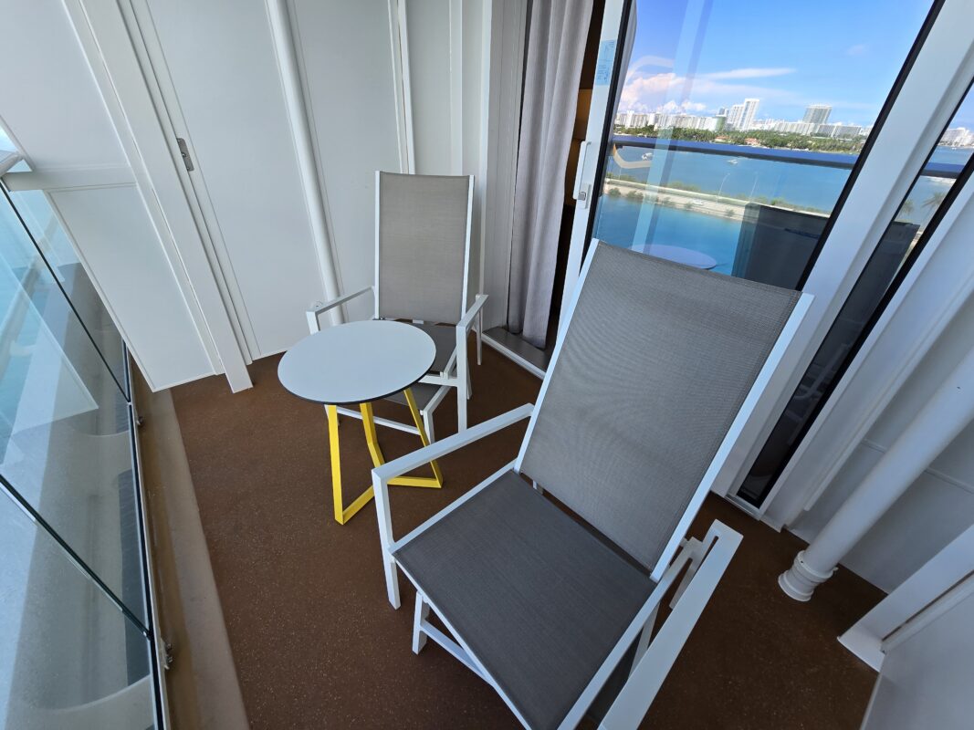 Private balcony on a cruise cabin featuring seating for two and a sea view through clear glass railing.