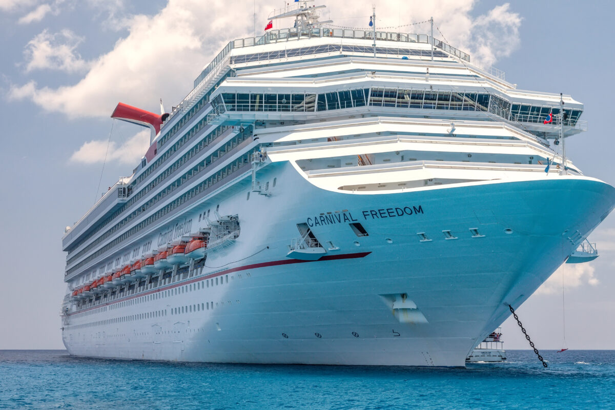 Close-up view of the cruise ship Carnival Freedom at anchor, showing the bow, upper decks, and large white hull above the blue water.