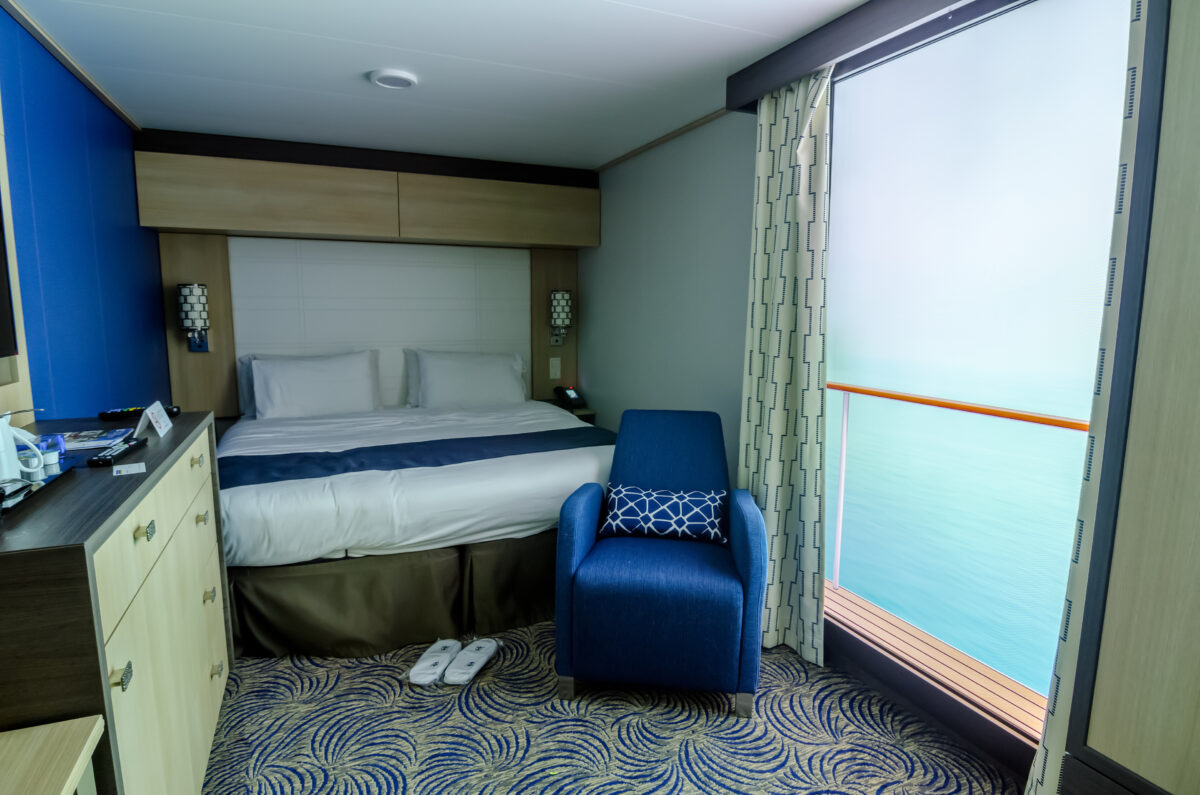 Modern inside stateroom featuring virtual balcony display, queen bed, and nautical-themed décor with blue accents.