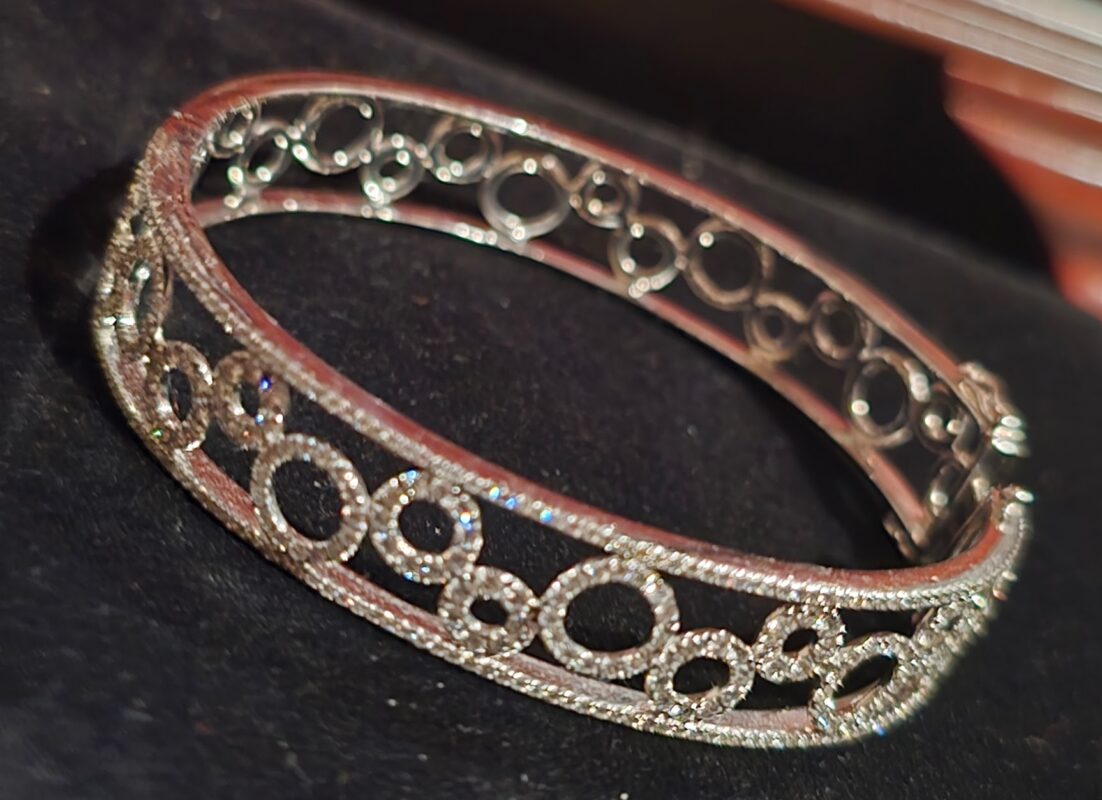 Close-up of an openwork diamond bangle bracelet with interlocking circles, resting on a dark display surface.
