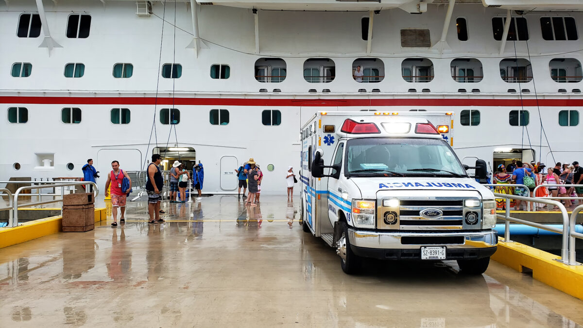 Emergency ambulance on a wet dock next to a cruise ship, illustrating shore-side medical transfer.