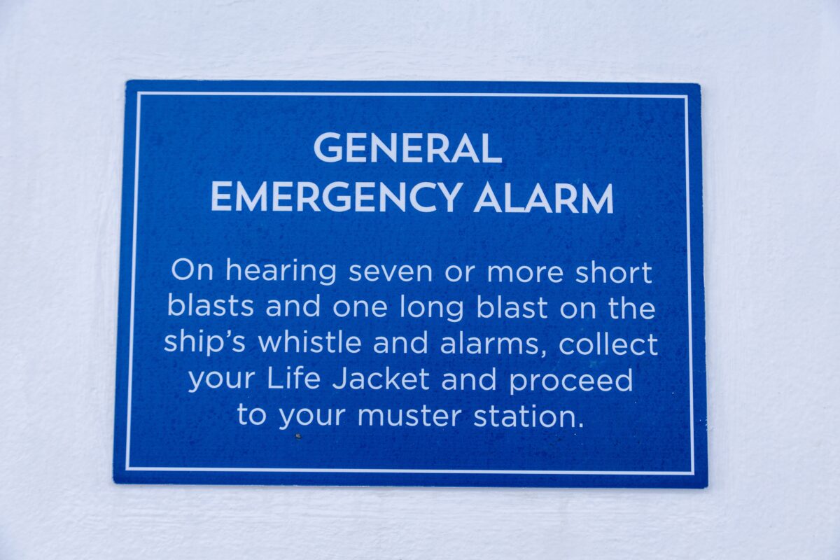 Close-up of a blue “General Emergency Alarm” safety sign with instructions to collect a life jacket and proceed to the muster station.