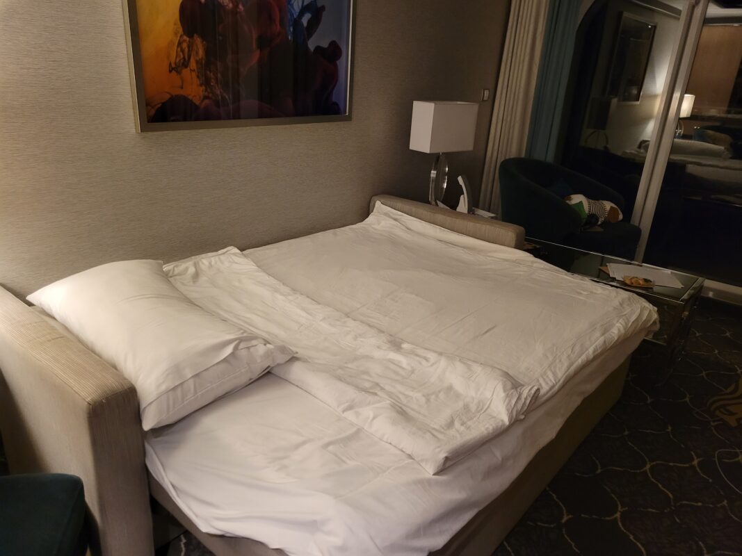 Interior of a cruise stateroom with the sofa converted into a bed, taking up part of the cabin’s sitting area.