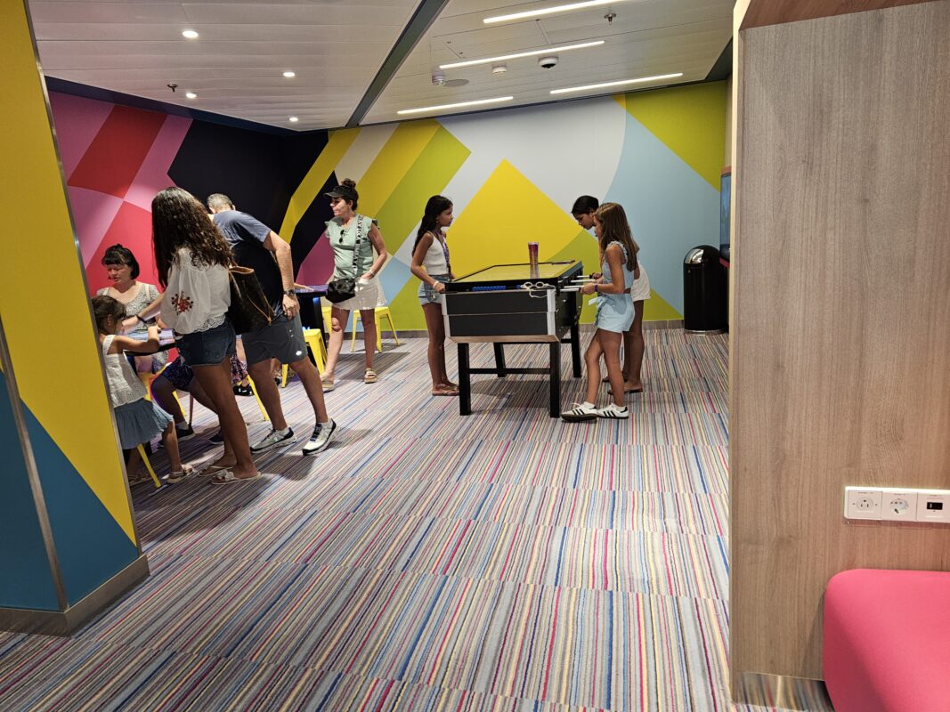 Families and children gathered inside a cruise ship kids’ club during an open house, with a foosball table and colorful wall mural.