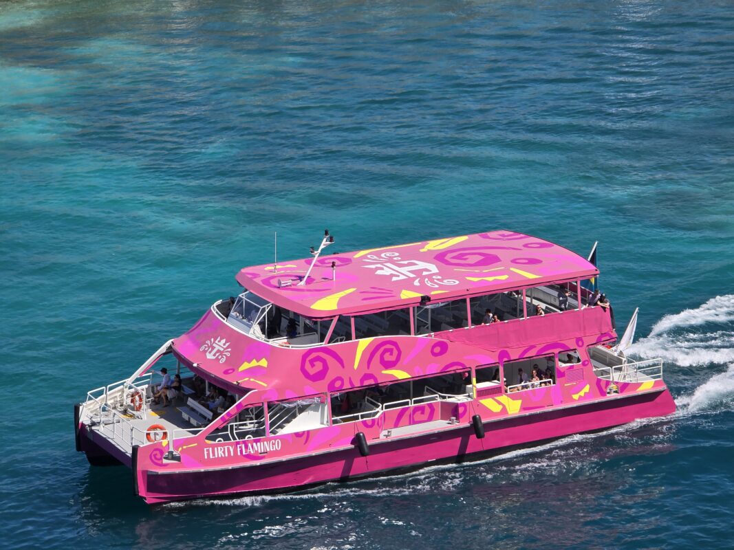 Bright pink Royal Caribbean ferry named Flirty Flamingo traveling across blue water in Nassau Harbor.