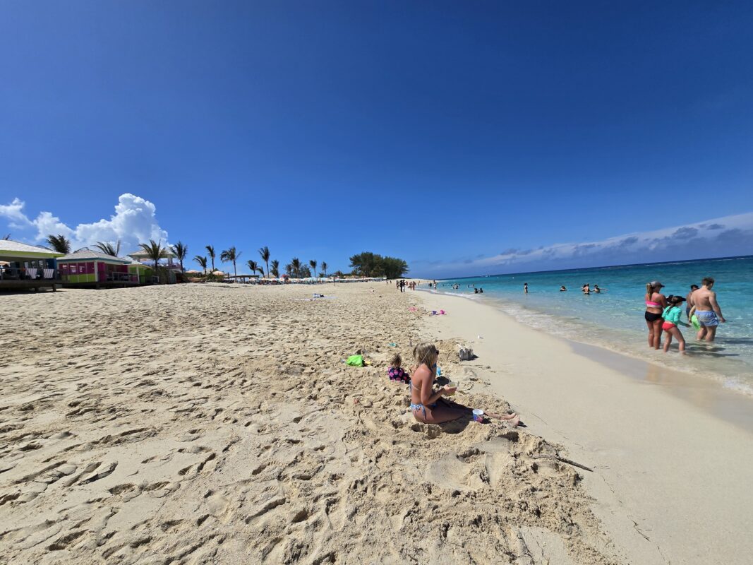 Family Beach at Royal Beach Club Paradise Island with a wide sandy shoreline, children playing in the sand, and guests wading in shallow water.
