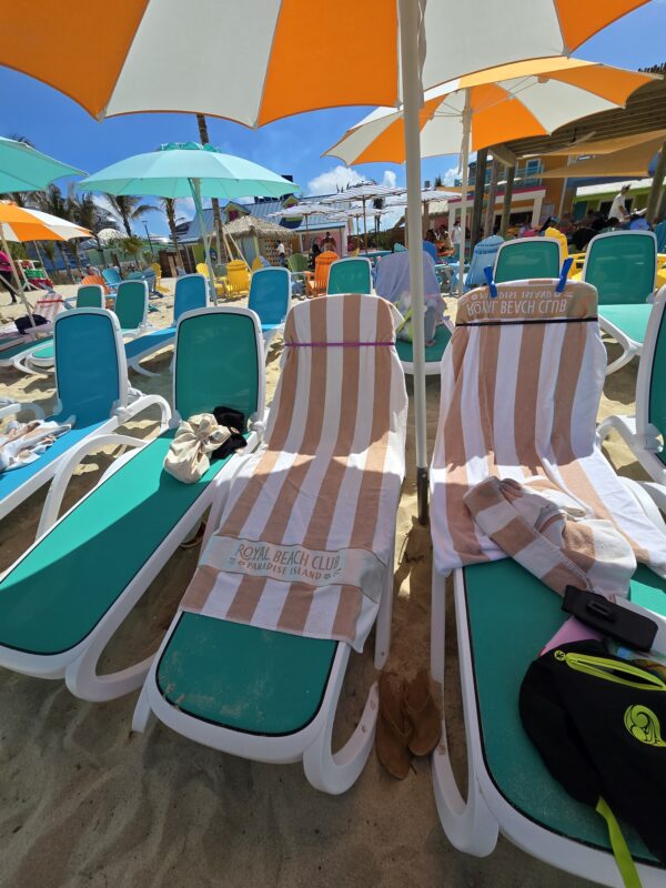 Beach loungers under umbrellas at Royal Beach Club Paradise Island with striped branded towels draped over the chairs.
