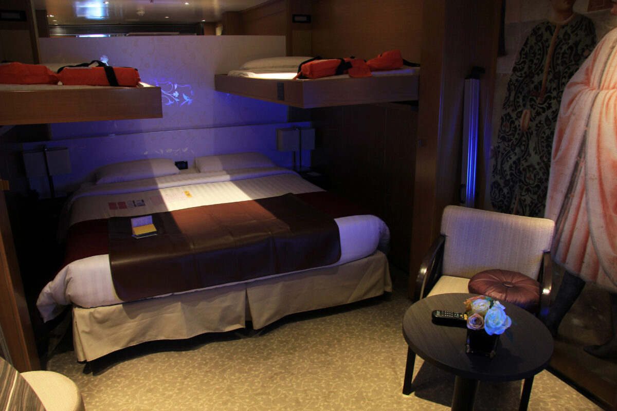 Cruise ship cabin with two Pullman beds lowered above a main bed, showing a sleep setup for up to four guests.