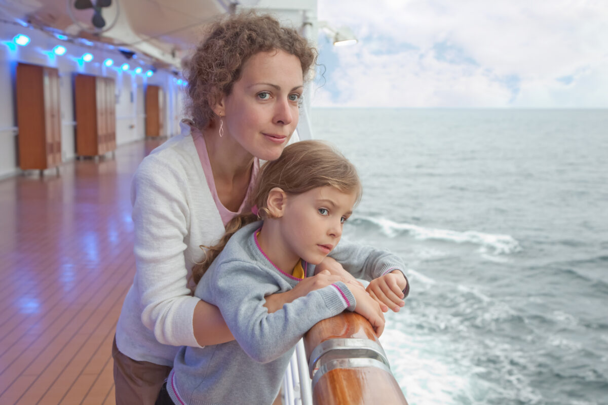 Woman and young girl leaning on a cruise ship railing while looking out over the ocean.