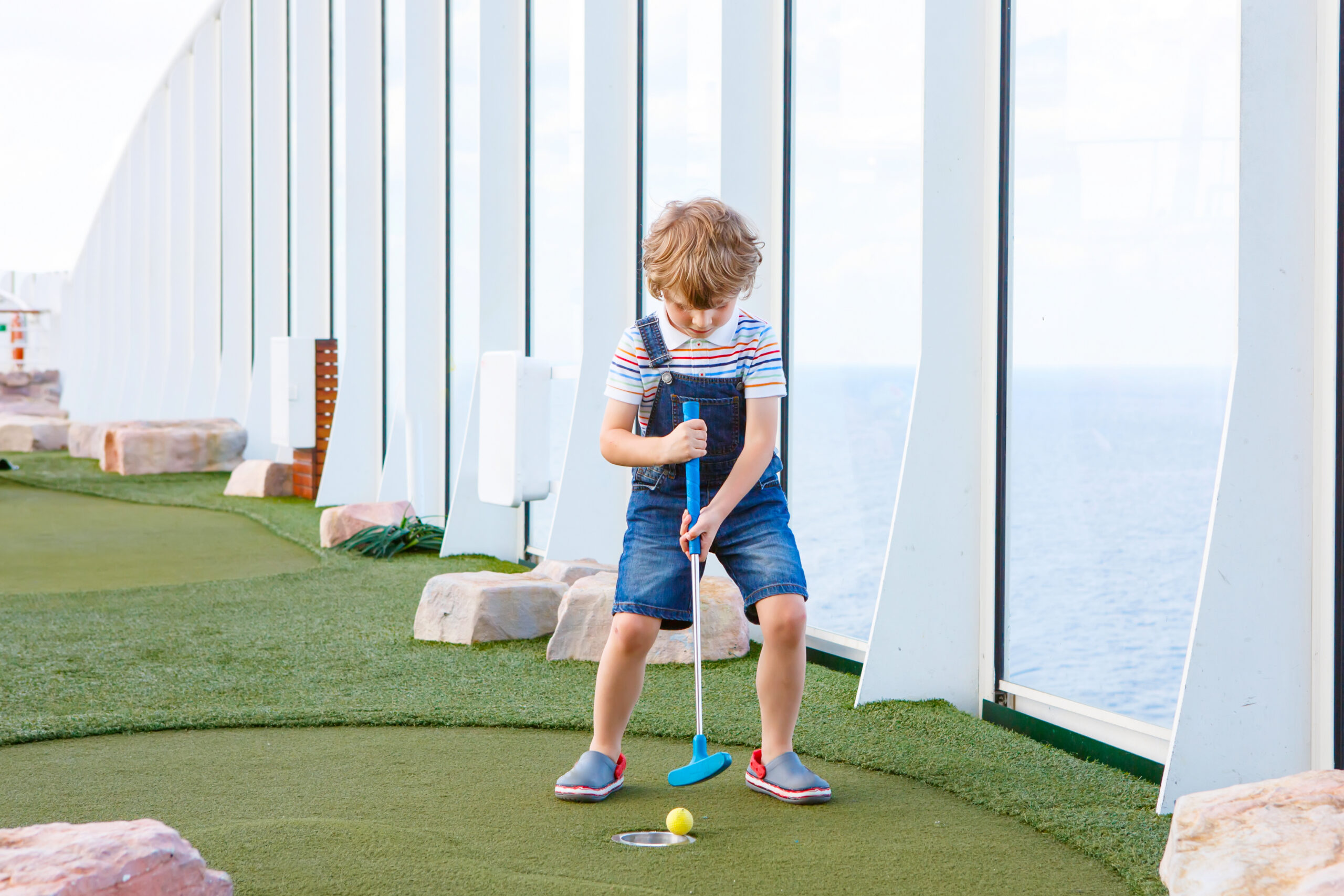 Young child playing mini golf on a cruise ship, illustrating first-time cruise tips for families choosing a ship with kid-friendly activities.