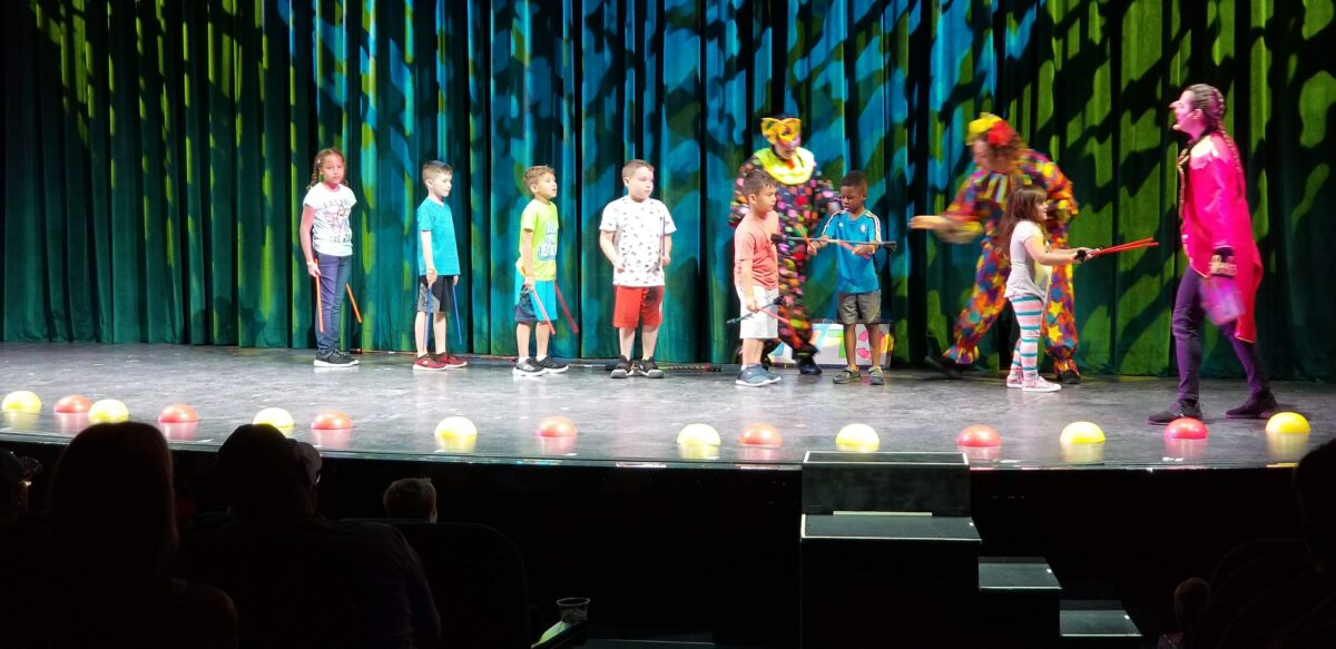 Kids participate in an onboard circus program on a theater stage during a family cruise.