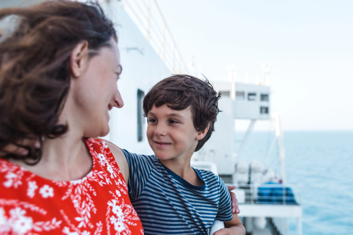 Woman and young boy stand together on a cruise ship with the ocean behind them, supporting a comparison of the best cruise lines for families.