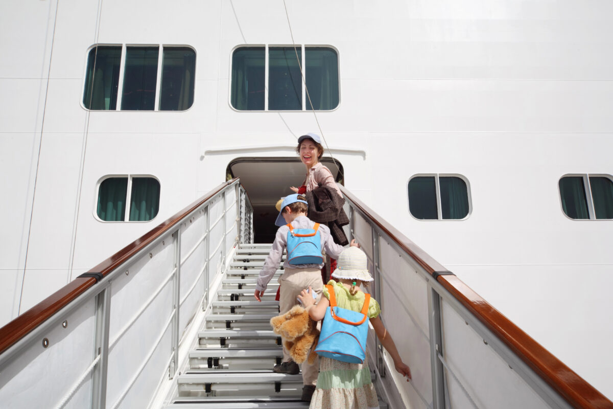Adult and 2 small children walk up a cruise ship ramp, suggesting a family trip planned for young kids.