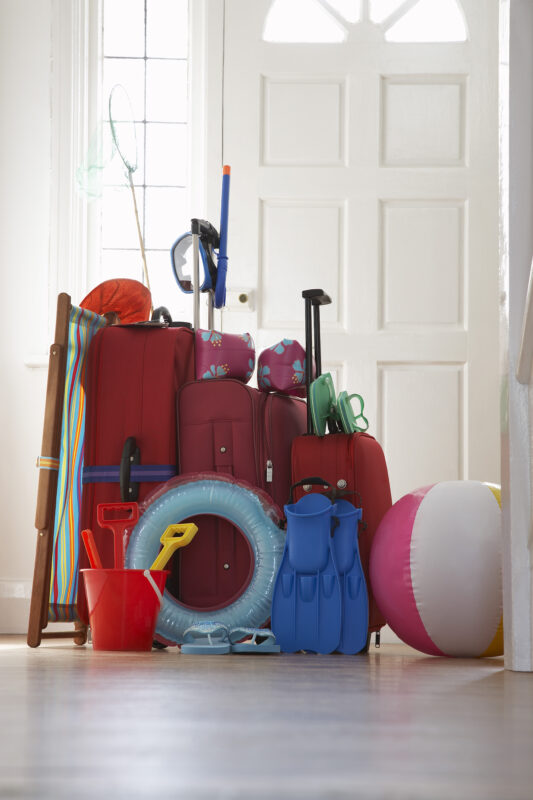 What to pack for a cruise | Three packed suitcases by a front door surrounded by an inflatable tube, swim fins, beach ball, bucket, and snorkel gear.