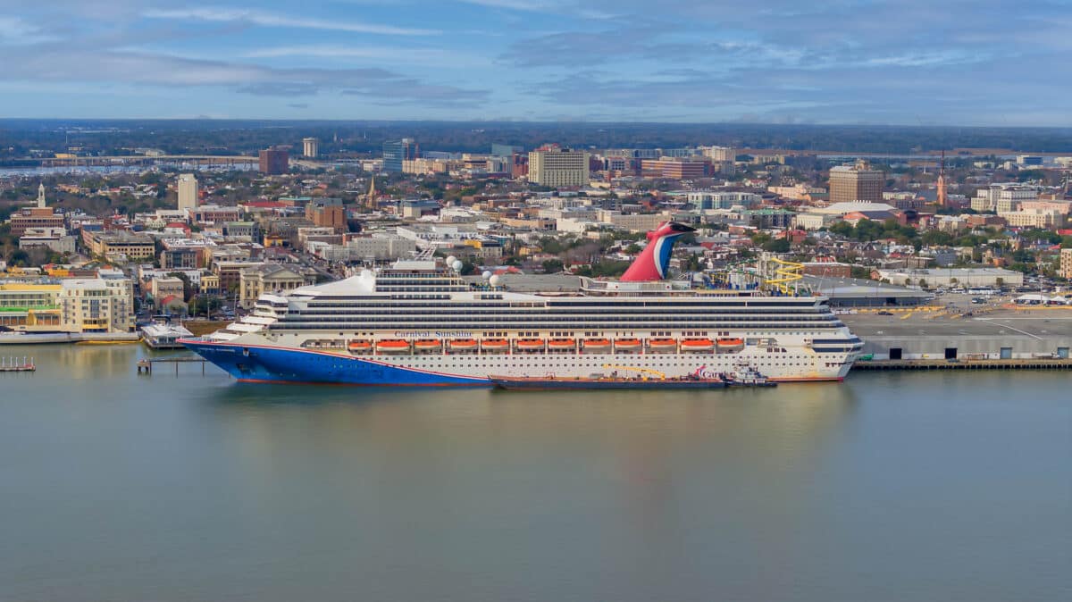Carnival Sunshine docked in South Carolina with its red funnel, waterslides, and city buildings visible.