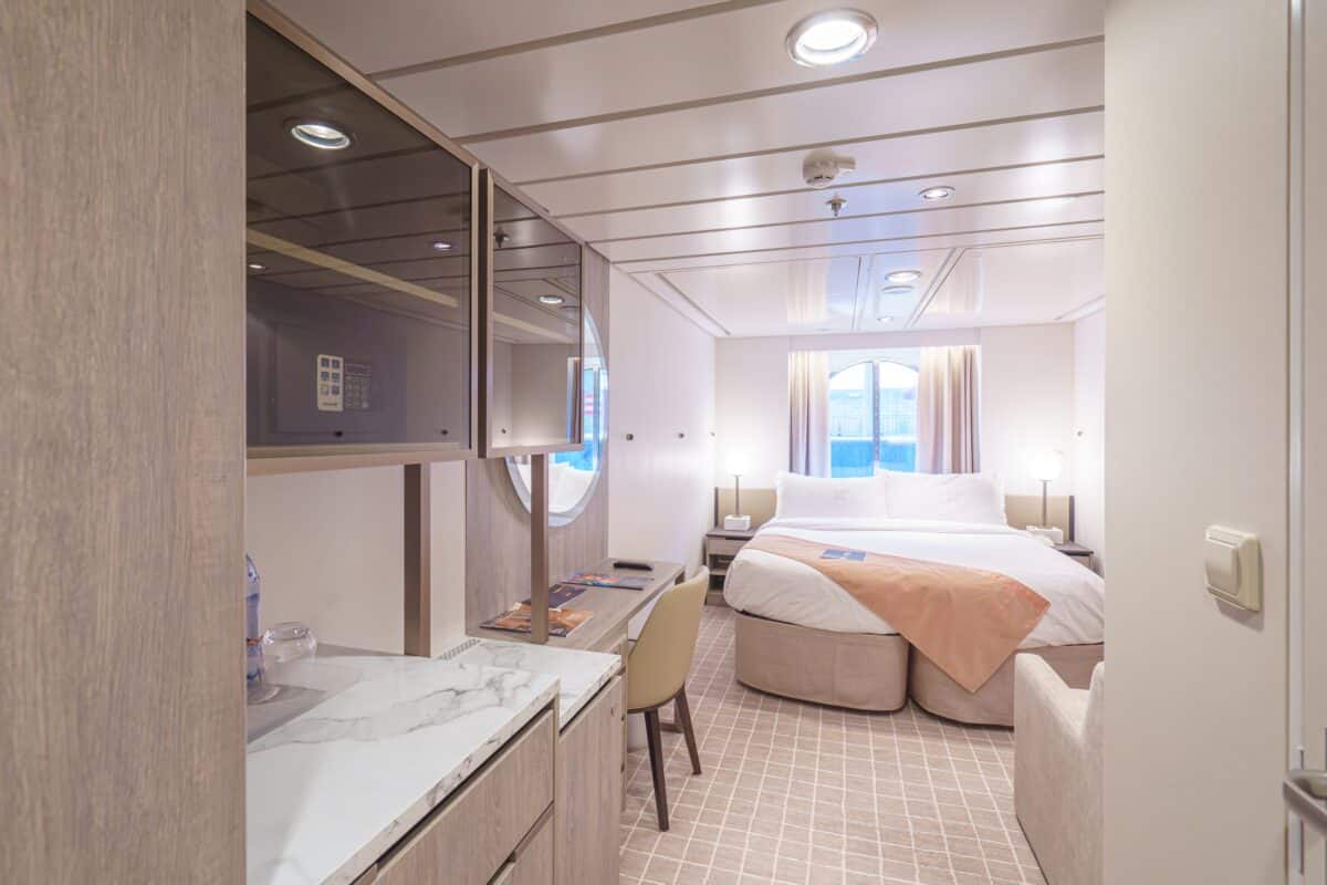 Interior of a renovated Celebrity Millennium stateroom with neutral décor, built-in storage, and a double bed.