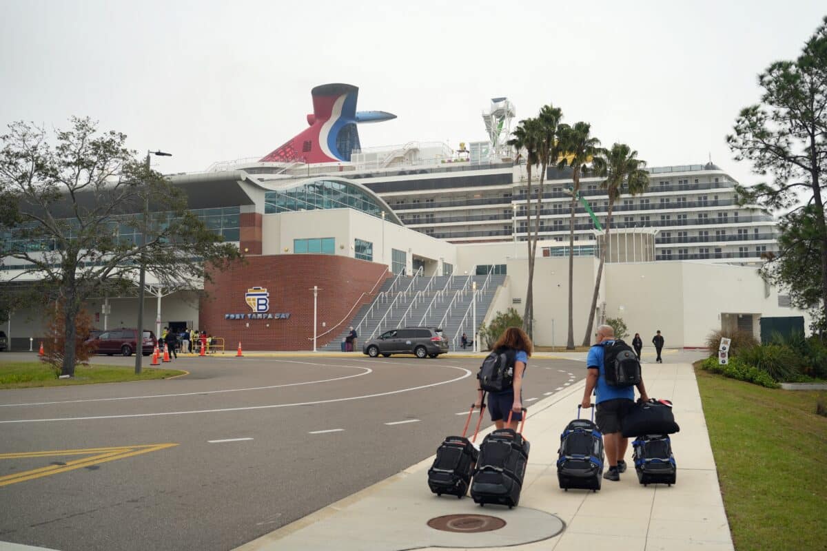 Old Cruise Ships | Couple walking towards terminal  with five pieces of luggage and two backpacks towards older Carnival ship at Tampa port.