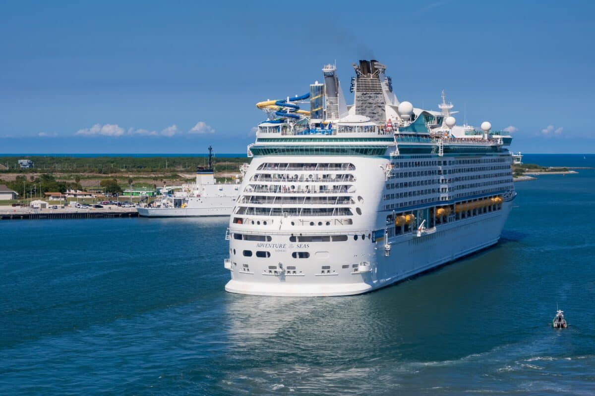 Older Royal Caribbean ship Adventure of the Seas viewed from behind as it sails away from port.